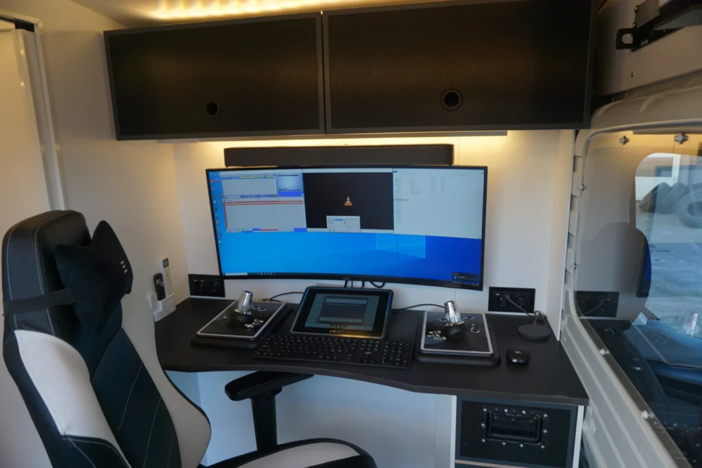 En moderne rørinspeksjonsbil har en sofistikert arbeidsstasjon med en buet skjerm som viser flere vinduer, tastatur, styrespaker, et nettbrett og en komfortabel stol. Dette velorganiserte oppsettet er perfekt utstyrt for avanserte teknologiske oppgaver.