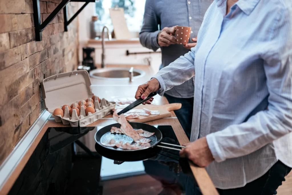 To personer lager frokost på kjøkkenet. Den ene er å steke bacon, og frigjøre en deilig duft som ligner på "matlukt fra nabo." En åpen kartong med egg ligger i nærheten. Den andre personen, som holder et krus, står ved siden av dem i det sjarmerende kjøkkenet i tre og murstein.