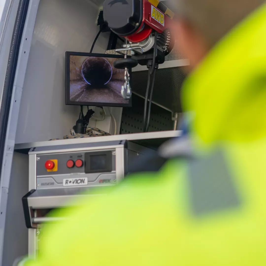 En person i gul jacka genomför en rörinspektion och observerar en monitor som avslöjar de intrikata detaljerna inuti ett rör.