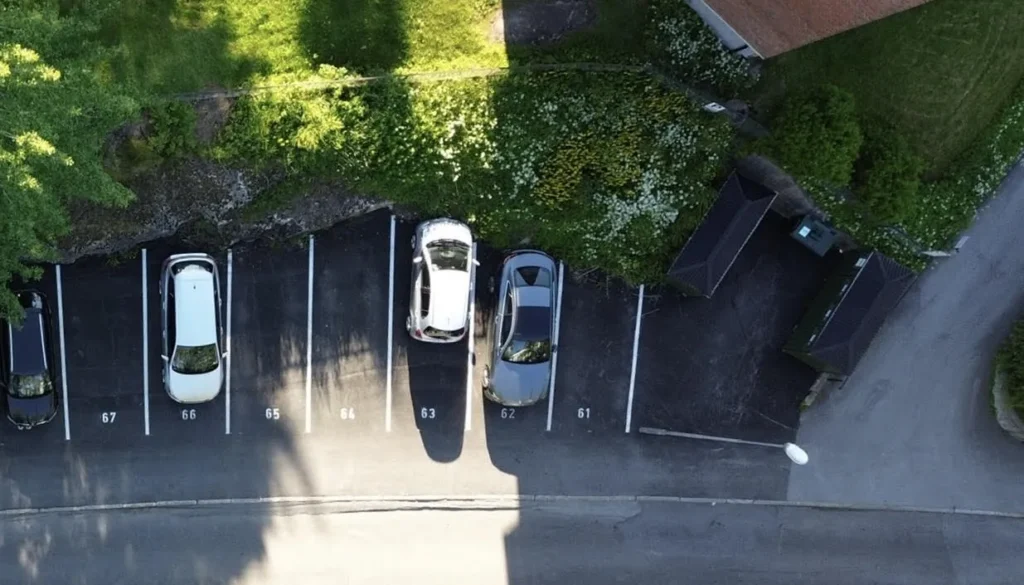 Luftfoto av en liten parkeringsplass ved siden av et gressområde og bygning viser et vellykket anleggsprosjekt. Fire biler er parkert.