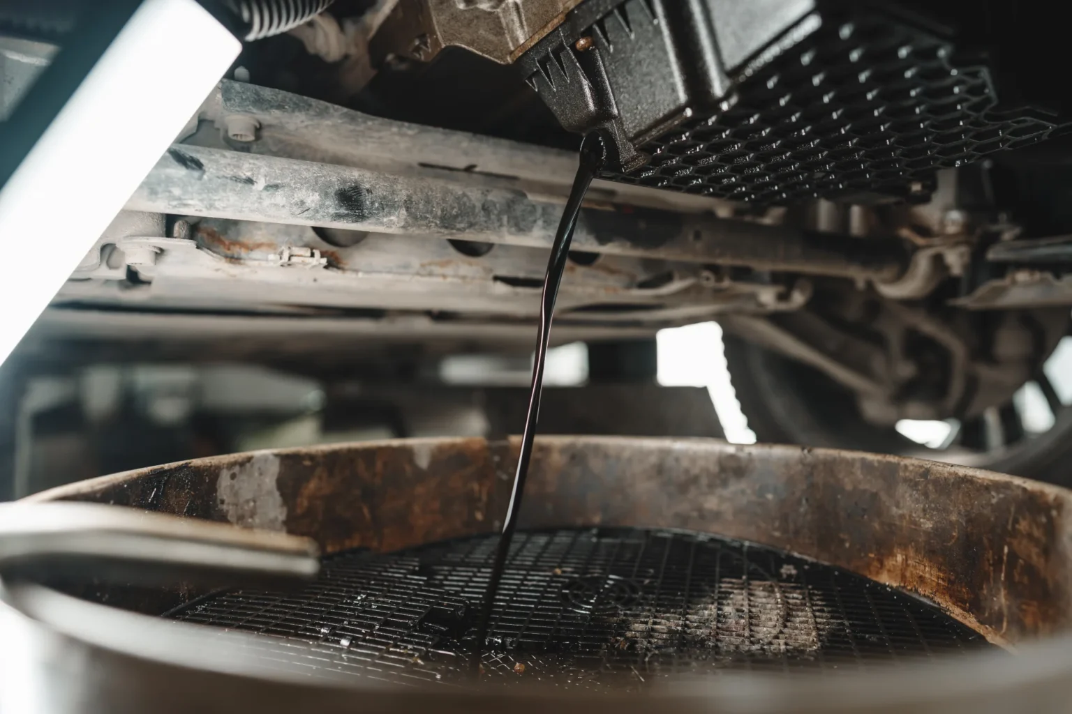 Svart motorolje renner fra en bils motor over i en panne utstyrt med en oljeavskiljare, og fremhever et oljeskift som pågår i en bilreparasjonsinnstilling.