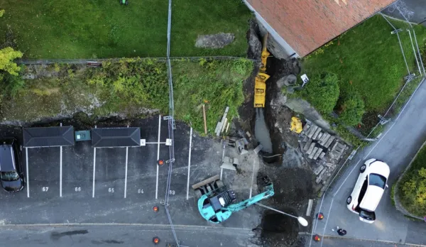 Luftfoto av en byggeplass i nærheten av en parkeringsplass og en bygning, med gravemaskiner som graver en grøft, spredt byggematerialer og flere parkerte biler i nærheten – som illustrerer noen vanlige problemer som ble møtt under utviklingen.