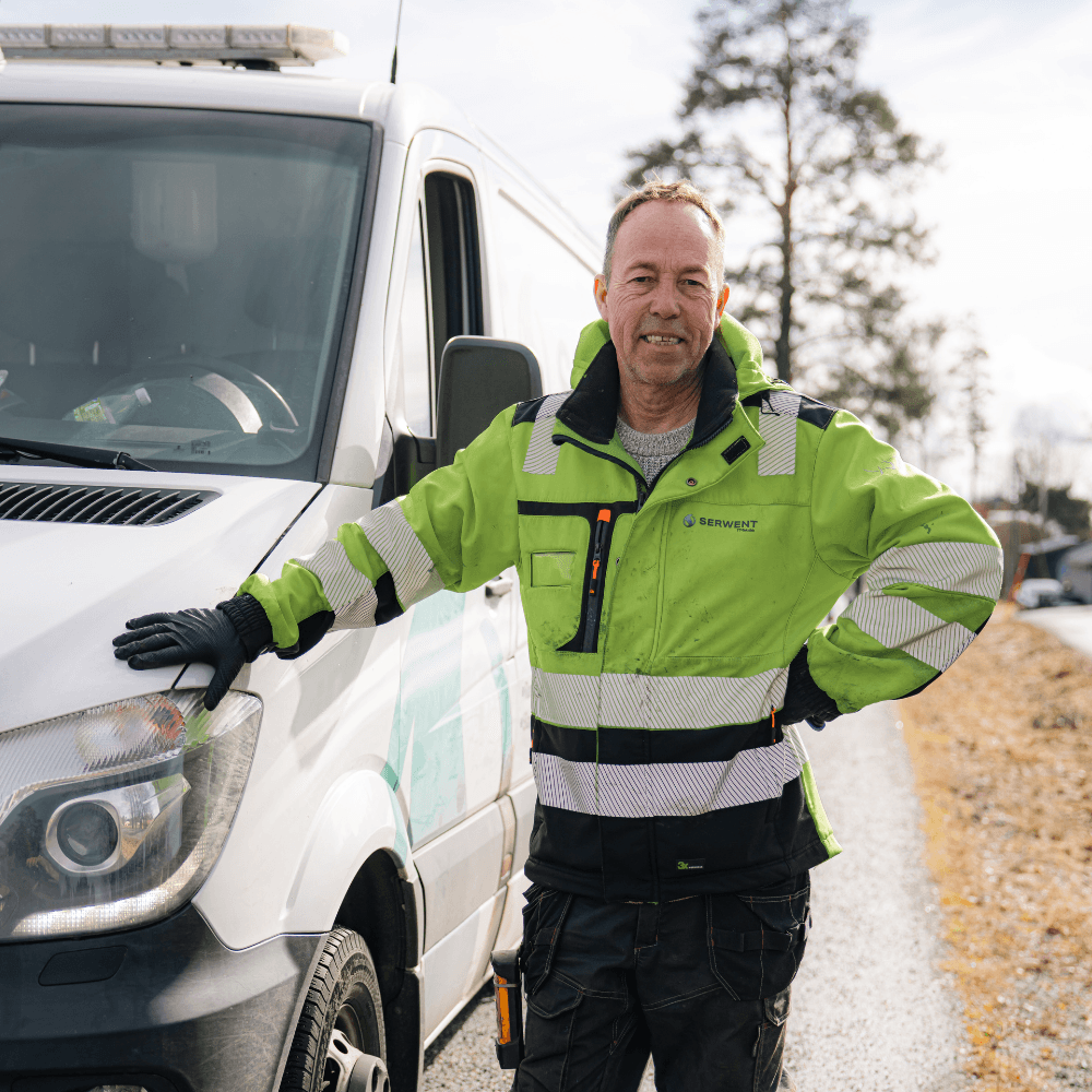 En smilende mann i en limegrønn arbeidsjakke med høy synlighet står lent mot en hvit servicebil.